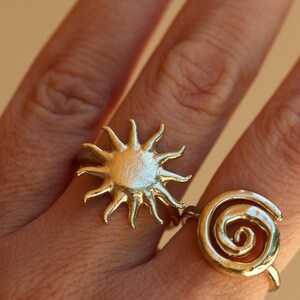 May include: Two gold rings on a finger. One ring is a sun design and the other is a spiral design.