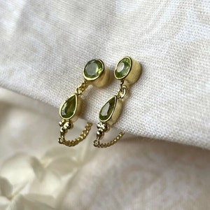 Peut inclure: Une paire de boucles d'oreilles en or avec des gouttes de pierres précieuses vertes. Les boucles d'oreilles présentent une pierre précieuse ronde en haut et une pierre précieuse en forme de larme qui pend en dessous.