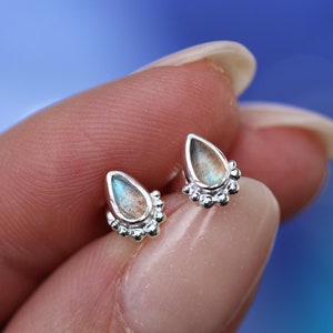 Peut inclure: Une paire de boucles d'oreilles en argent en forme de larme avec une petite pierre précieuse irisée au centre de chaque larme. Les boucles d'oreilles sont serties d'une rangée de petites perles d'argent autour de la pierre précieuse.