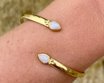 May include: A gold bracelet with two teardrop-shaped moonstone accents.