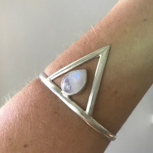 May include: A silver triangle cuff bracelet with a teardrop-shaped moonstone in the center.