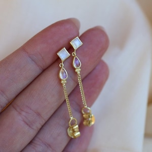 May include: A pair of gold dangle earrings with a square moonstone and a teardrop moonstone on each earring.