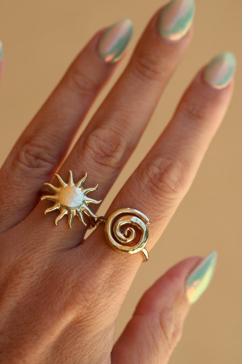 May include: Two gold rings on a finger. One ring is a sun design and the other is a spiral design.