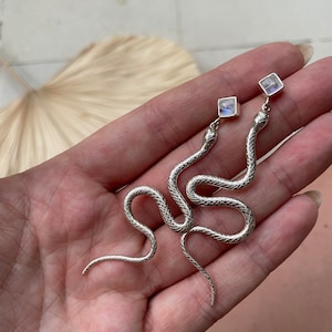 May include: A pair of silver snake earrings with a square moonstone gemstone at the end of each snake.