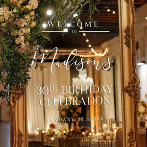 May include: A gold-framed mirror with a white sign that reads "Welcome to Madison's 30th Birthday Celebration January 19, 2024". The mirror is decorated with a floral arrangement of pink and cream roses.