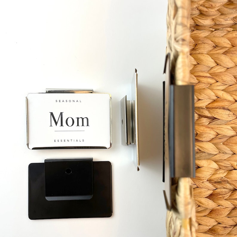 Puede incluir: Un portaetiquetas plateado con el texto "SEASONAL Mom ESSENTIALS" sobre un fondo blanco. El portaetiquetas est&aacute; unido a un soporte met&aacute;lico negro.