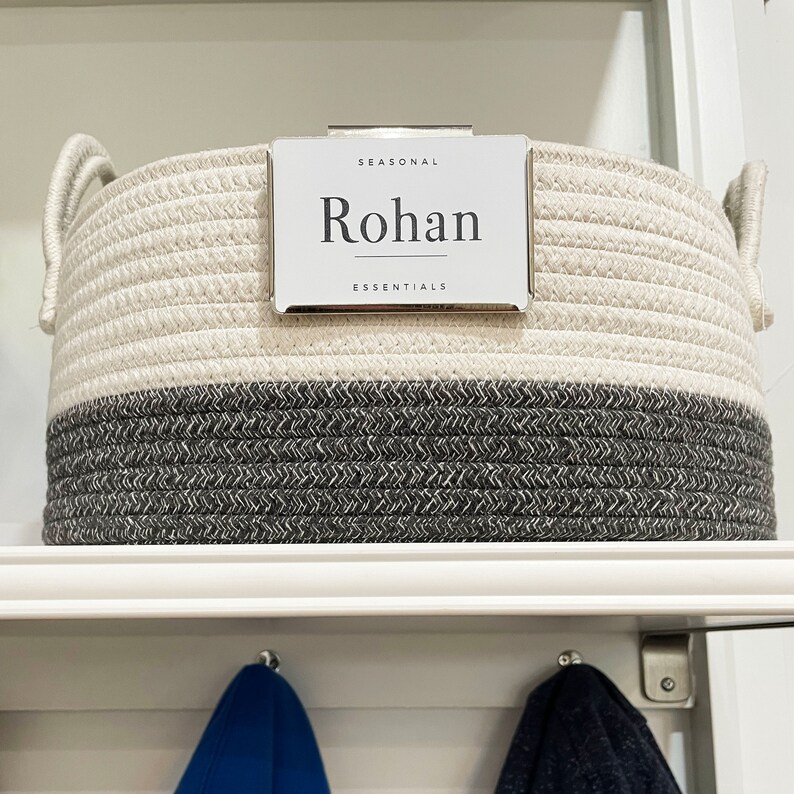 Puede incluir: Una cesta de almacenamiento de cuerda blanca y gris con una etiqueta plateada que dice "SEASONAL Rohan ESSENTIALS".