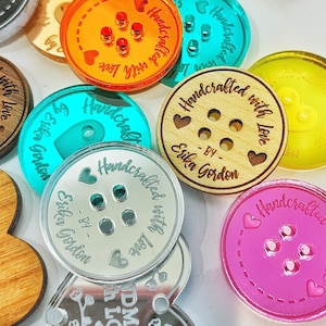 May include: A collection of circular and heart-shaped buttons in various colours including orange, yellow, pink, teal, silver, and wood grain. Each button features four holes and the engraved text Handcrafted with love by Erika Gordon.