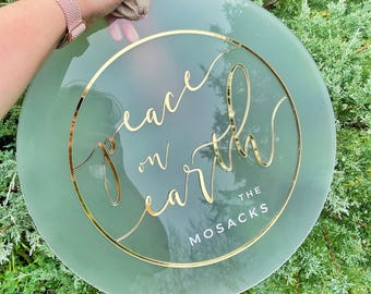 Colgante de puerta principal personalizado con el nombre de la familia "Paz en la Tierra" y corona de texto 3D minimalista.