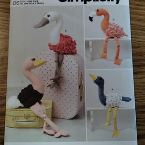 May include: Simplicity sewing pattern S9774 for stuffed birds. The envelope features illustrations of four plush bird designs with long legs, including a white swan, a pink flamingo, a pink ostrich, and a blue bird, all with textured plumage.
