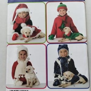 May include: A Simplicity sewing pattern envelope 3973 featuring illustrations of children and dogs wearing matching holiday-themed hats, scarves, and capes in red, green, white, and blue colours with pom-pom accents and snowflake patterns.