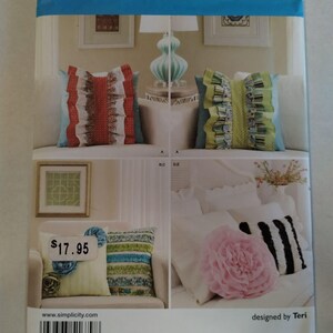 Puede incluir: Un sobre de patrón de costura Simplicity 1679 para cojines decorativos. La parte frontal muestra varios diseños de cojines con volantes, motivos florales y rayas en rojo, verde, azul, rosa y negro. El texto incluye Simplicity 1679.