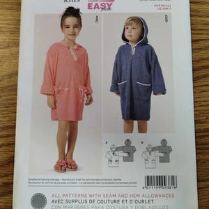 May include: A Burda Kids sewing pattern envelope 9381 for a hooded bath robe. The front shows two children wearing the finished robe in coral and navy blue, with front pockets and ties. Includes sizing information for EUR 88-122 and US 18M-7.