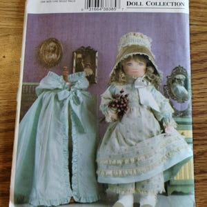 May include: A Vogue Doll Collection sewing pattern, V7923, featuring a doll in a light blue dress and bonnet, holding flowers. The pattern includes a matching cape. The cover is light purple with text and illustrations.