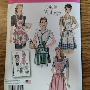 May include: A Simplicity sewing pattern envelope 1221 A for 1940s style aprons. The front displays four illustrations of aprons labeled A, B, C, and D, featuring floral, striped, and solid designs. Includes a barcode, text, and a small inset image.