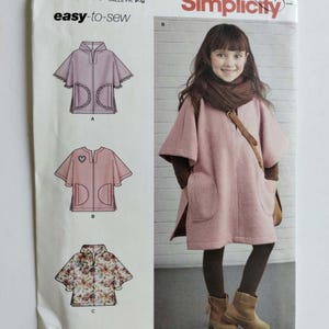 May include: Simplicity sewing pattern 8428 for an easy-to-sew poncho with three variations. The envelope features illustrations of the garment designs and a photograph of a person wearing a pink poncho with pockets and a brown scarf.