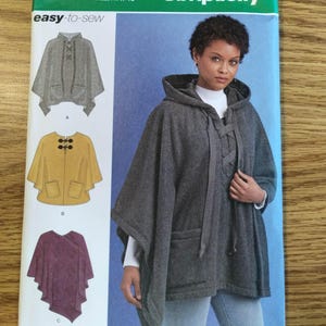 Peut inclure: Patron de couture Simplicity 8517 pour un poncho à capuche facile à coudre. L'enveloppe présente trois variantes : un poncho gris à capuche avec laçage, un poncho jaune avec fermetures à bascule et un poncho asymétrique violet. Tailles XS-XL.