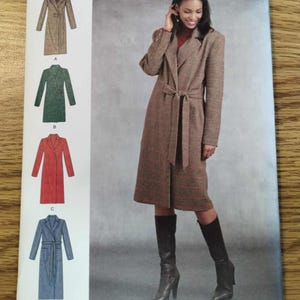 Può includere: Cartamodello Simplicity 8796 per un cappotto a maniche lunghe al ginocchio con colletto a revers e cintura da annodare. La busta mostra quattro varianti del cappotto in marrone, verde, rosso e blu, con le taglie europee 42-50 chiaramente indicate.