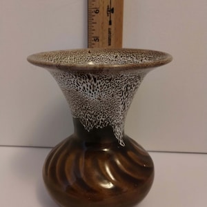 May include: A ceramic vase with a brown, swirling base and a flared rim featuring a white speckled glaze. A wooden ruler is positioned behind the vase, showing the top edge of the rim reaches approximately 7.25 inches in height.
