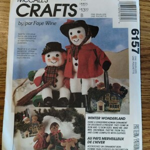 May include: A McCall's Crafts sewing pattern envelope 6157 by Faye Wine featuring illustrations of two snowmen figures, one standing and one sitting, and gingerbread ornaments. The text includes Winter Wonderland and 70cm tall for snowmen.