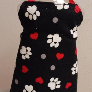 May include: A black fabric bottle cover with white paw prints and red hearts. The cover is designed to fit a standard size soap bottle.