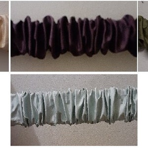 May include: Five fabric samples in different colors: beige, purple, green, light blue, and dark green. The fabric is gathered and ruffled, creating a decorative trim.