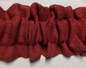 May include: Close-up of a ruffled, burgundy-colored burlap fabric. The fabric is tightly woven and has a textured appearance. The ruffled design adds a decorative element, suitable for home decor or craft projects.