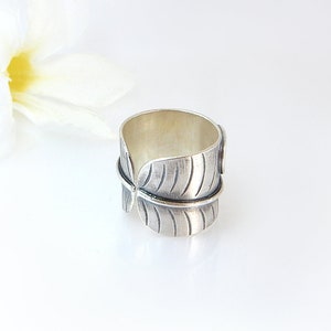 Op de afbeelding: Een zilveren ring met een bladontwerp. De ring is breed en heeft een getextureerd oppervlak.