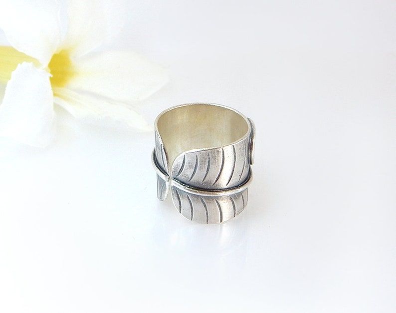 Op de afbeelding: Een zilveren ring met een bladontwerp. De ring is breed en heeft een getextureerd oppervlak.
