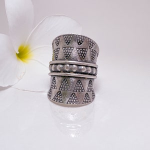 May include: A silver ring with a geometric pattern of triangles and dots. The ring is wide and has a band of small beads around the middle.