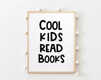 Könnte beinhalten: Ein gerahmter Druck mit dem Text "Cool Kids Read Books" in schwarzen Buchstaben auf weißem Hintergrund. Der Druck hängt an einer weißen Wand mit einer Schnur aus weißen Pompons auf jeder Seite.