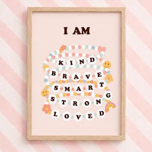 Peut inclure: Une affiche encadrée sur fond rose clair avec le texte I AM en lettres marron foncé au-dessus d'un graphique de cordons de perles colorées disposés en rangées. Les perles forment les mots KIND, BRAVE, SMART, STRONG et LOVED.