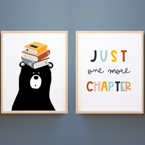 May include: Two framed prints featuring a black bear wearing a stack of colourful books on its head and the text "JUST one more CHAPTER" in colourful letters.