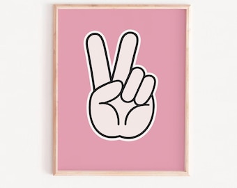 Op de afbeelding: Een ingelijste print met een hand die het vredesteken maakt. De witte hand met zwarte contouren staat tegen een roze achtergrond. De lijst heeft een lichte houtkleur.