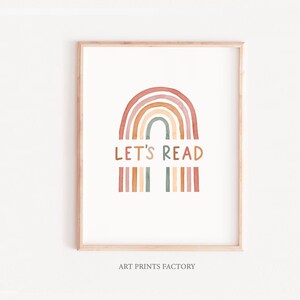 May include: A printable art print featuring a rainbow with a watercolor effect in shades of orange, brown, and green. The text "LET'S READ" is written in a whimsical font below the rainbow. The print is framed in a light wood frame.