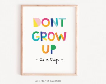 May include: A colorful framed print with the text "DON'T GROW UP - it's a trap -" in a playful font. The letters are made up of different colored shapes. The print is on a white background and has a light wood frame.