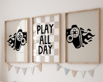 May include: Three framed prints with a gaming theme. The center print has a checkered background and the text "PLAY ALL DAY". The prints on either side feature a black and white illustration of a video game controller with flames.