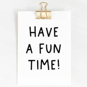 May include: A white card with black text that reads "Have a fun time!" The card is attached to a white wall with a gold paper clip.
