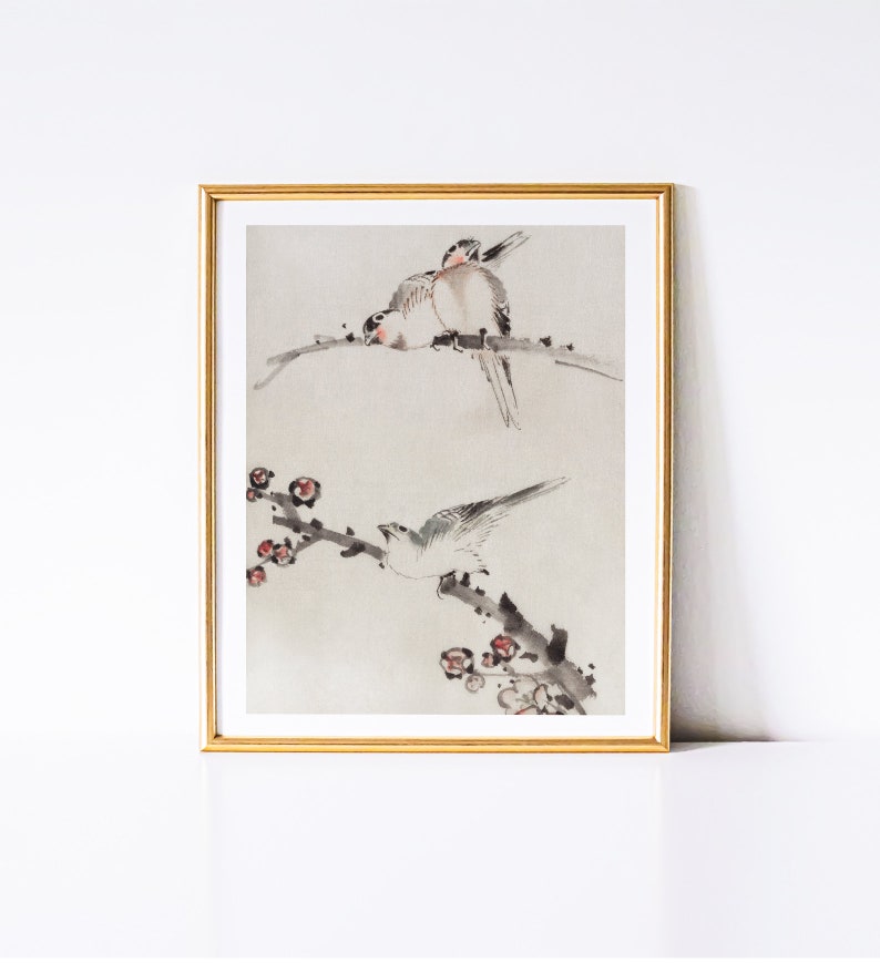 May include: A framed watercolor painting of two birds perched on a branch with delicate pink blossoms. The birds are painted in shades of gray and white, with subtle details of their feathers. The background is a soft, muted gray.