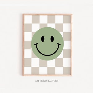 May include: A green smiley face on a beige and white checkered background. The print is framed with a light wood frame.