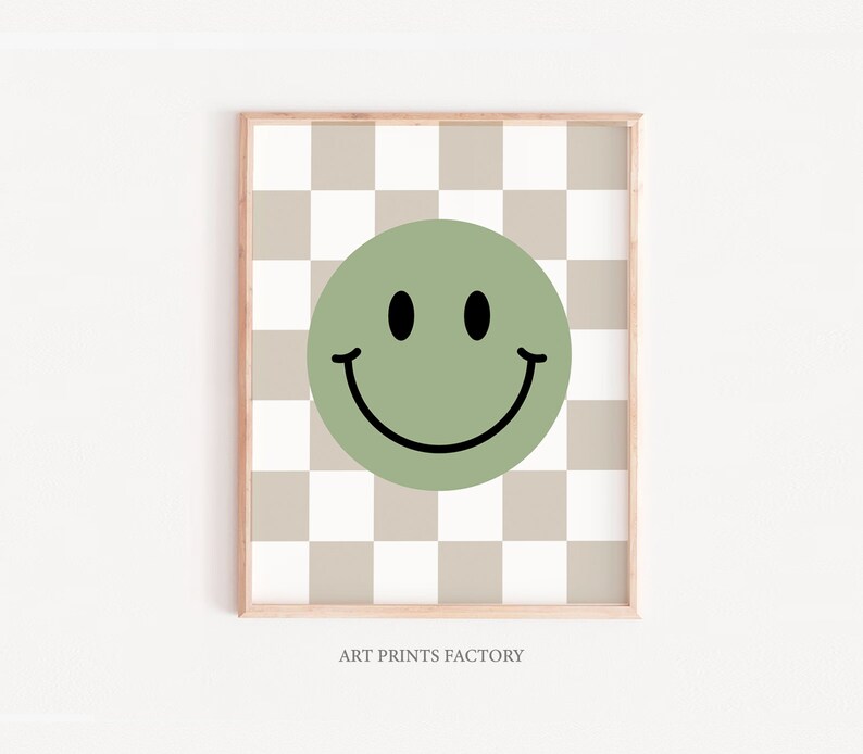 May include: A green smiley face on a beige and white checkered background. The print is framed with a light wood frame.
