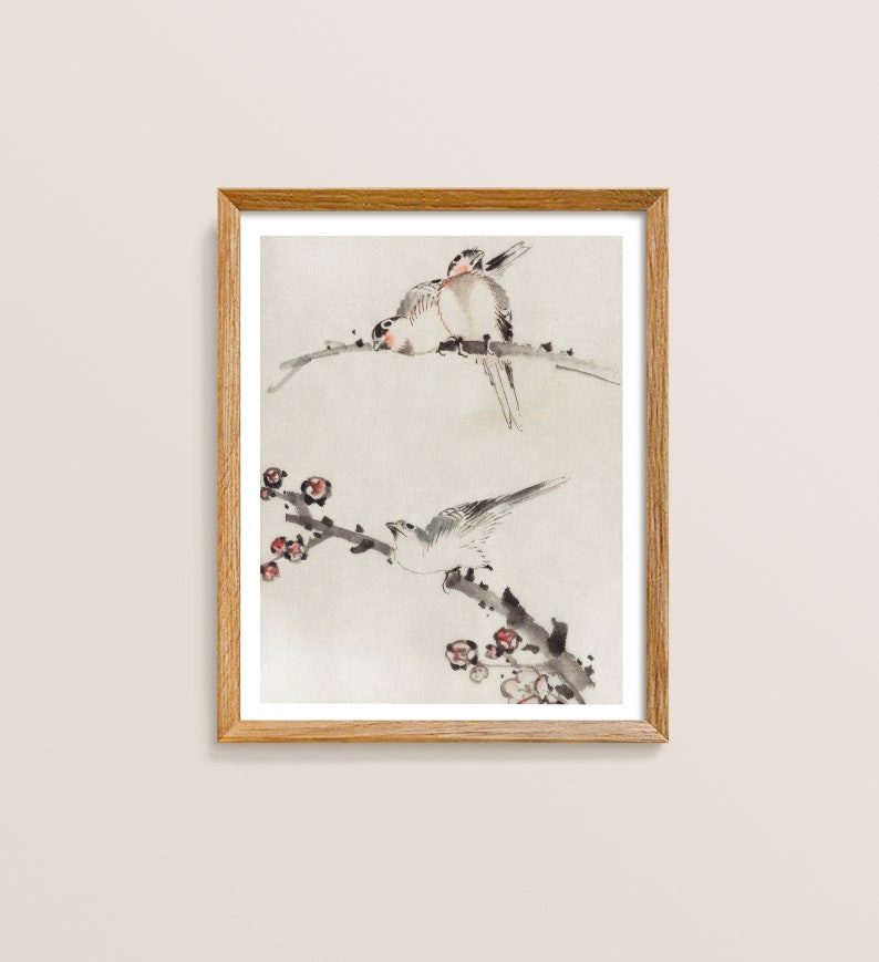 May include: A framed watercolor painting of two birds perched on a branch with delicate pink blossoms. The birds are painted in shades of gray and white, with subtle hints of pink and brown. The background is a soft, light gray.