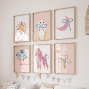 May include: Six framed art prints with a pale pink backdrop. The prints showcase watercolour illustrations of a sun, a cat with a bow, a crescent moon, a bouquet of flowers, a poodle, and an ice cream cone. The frames are made of light wood.