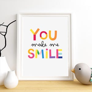 Puede incluir: Una impresi&oacute;n enmarcada en blanco con el texto "YOU make me SMILE" en letras geom&eacute;tricas de colores. Las letras son en tonos de rojo, naranja, amarillo, verde, azul y morado.