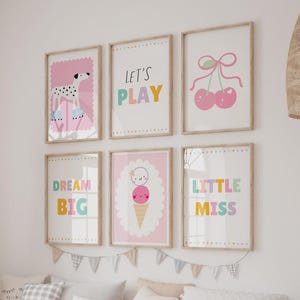 May include: A set of six framed wall art prints featuring colorful illustrations of a dalmatian, cherries, and an ice cream cone, alongside text that reads LET'S PLAY, DREAM BIG, and LITTLE MISS, all displayed in light wood frames on a white wall.