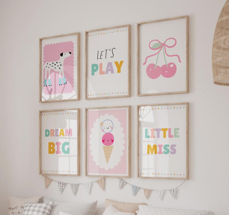 May include: A set of six framed wall art prints featuring colorful illustrations of a dalmatian, cherries, and an ice cream cone, alongside text that reads LET'S PLAY, DREAM BIG, and LITTLE MISS, all displayed in light wood frames on a white wall.