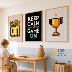 Puede incluir: Tres l&aacute;minas de pared enmarcadas con dise&ntilde;os de arte de p&iacute;xeles. La l&aacute;mina de la izquierda muestra el texto GAME ON en amarillo. La central muestra el texto KEEP CALM AND GAME ON en blanco y turquesa. La derecha muestra un trofeo pixelado dorado.