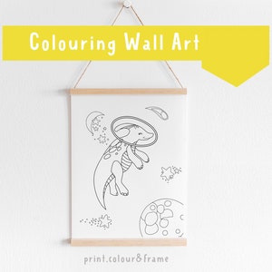 May include: Black and white line art print of a dinosaur wearing a space helmet and floating in space. The dinosaur is surrounded by stars and a crescent moon. The print is framed and ready to be colored in.