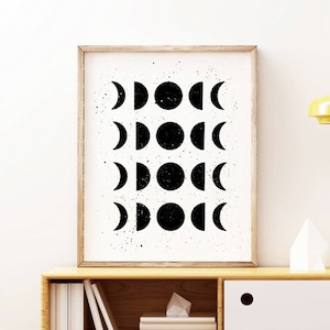 May include: Black and white print of a moon phases design in a wooden frame. The print features a white background with black moon phases in different stages.