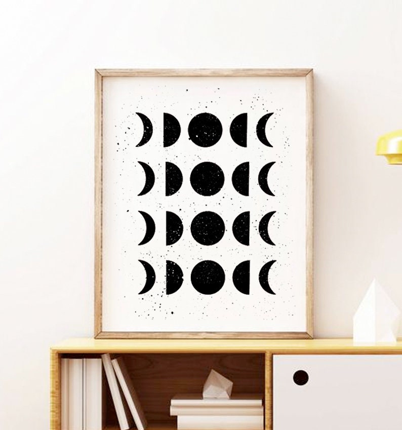 May include: Black and white print of a moon phases design in a wooden frame. The print features a white background with black moon phases in different stages.